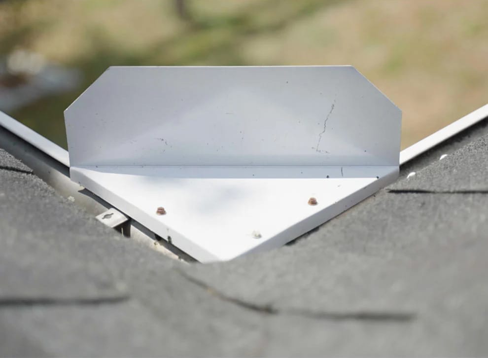 A metal roof flashing is installed at the intersection of two shingle roof sections, secured with screws.
